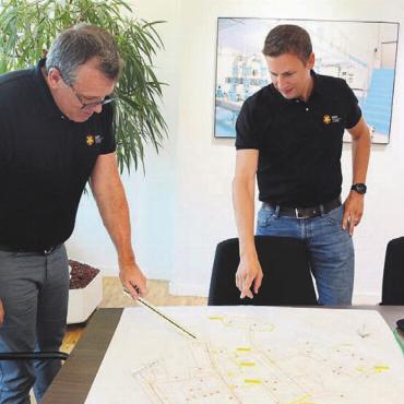 Wärme aus eigenen Wäldern - Geschäftsführer Martin Hössli (links) und Projektleiter Jonas Moos mit den Plänen des Verteilnetzes, das immer mehr konkretisiert wird. Bilder: chh