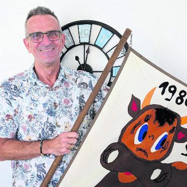 Auf den Schlitten gebracht - Guido Wirth mit der 1980 selbst gebastelten Fahne seines allerersten Klassenlagers als Lehrer. Im Hintergrund die Uhr, die er nach der Räumung seines Büros bewusst als Letztes abhängen will. Bild: Marco Huwyler
