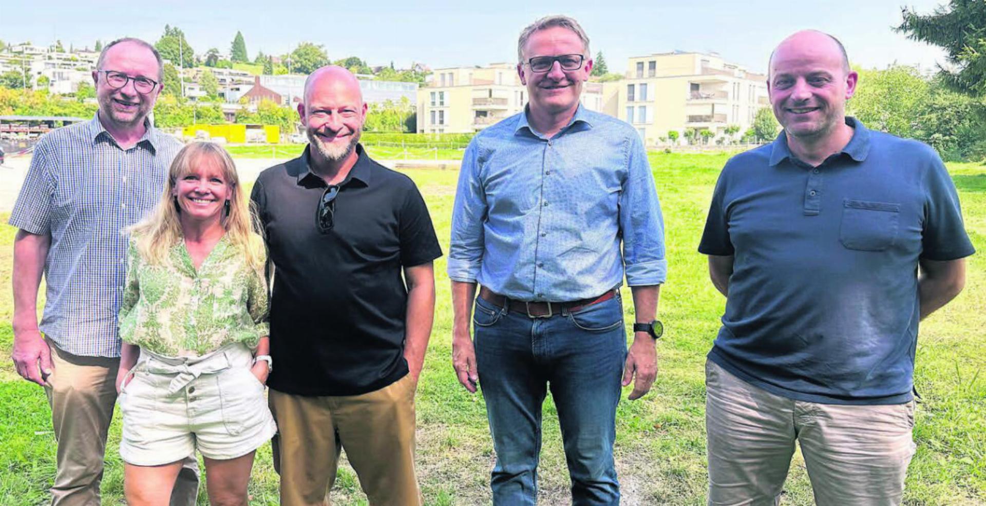 Auf dem Gelände rund um das Merkur-Areal im Hintergrund sollen die Festivitäten stattfinden. Diese fünf bilden einen Teil des OK der 850-Jahr-Feier 2028. Von links: Beat Koch, Romana Kammer, die beiden OK-Präsidenten Dennis Andermatt und Arsène Perroud – und Martin Laubacher. Bild: Stefan Sprenger